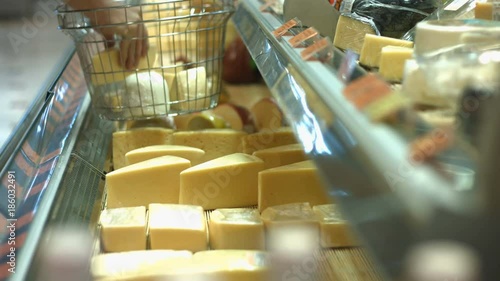 Cheese on the shelf in the supermarket.
Horizontal ( from right to left ) pan.
The man's hand takes two pieces of cheese from the shelf and puts them in the basket.
