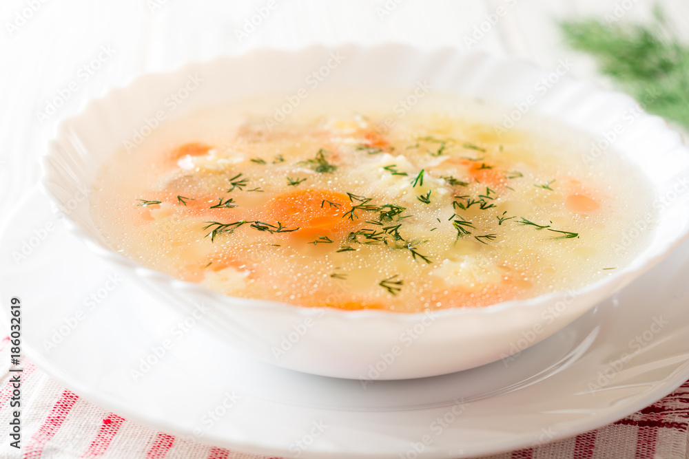 Chicken soup with stelline pasta and carrot on white wooden table.