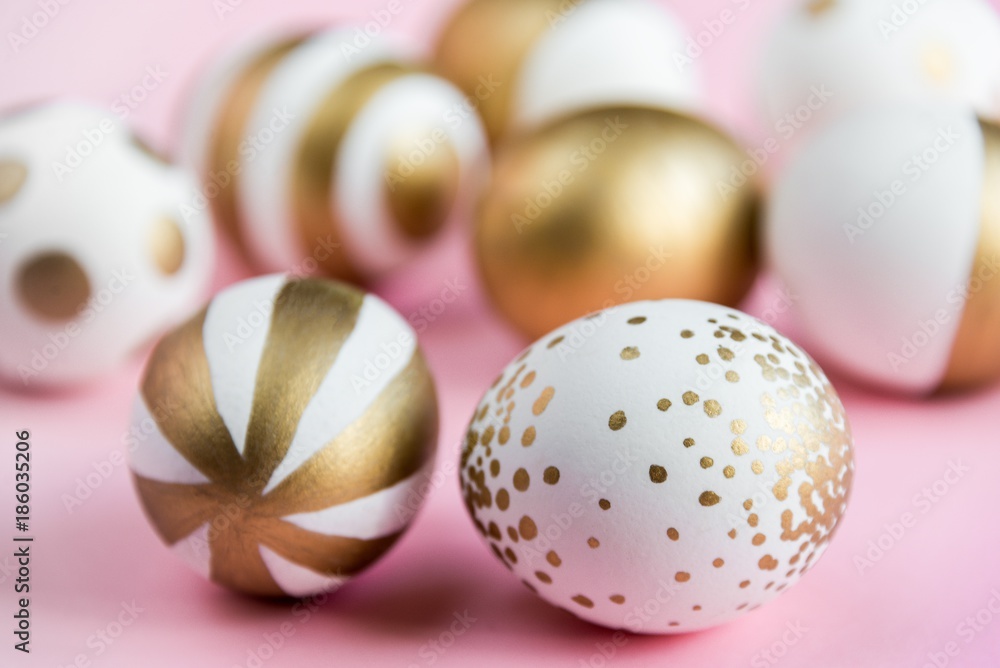 Top view of easter eggs colored with golden paint. Various striped and dotted designs. Pink background.