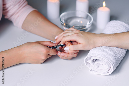 Nails beauty. Woman hands receiving nail care treatment by professional manicure specialist in nail salon. Manicurist cutting cuticle on nails with nail clippers.