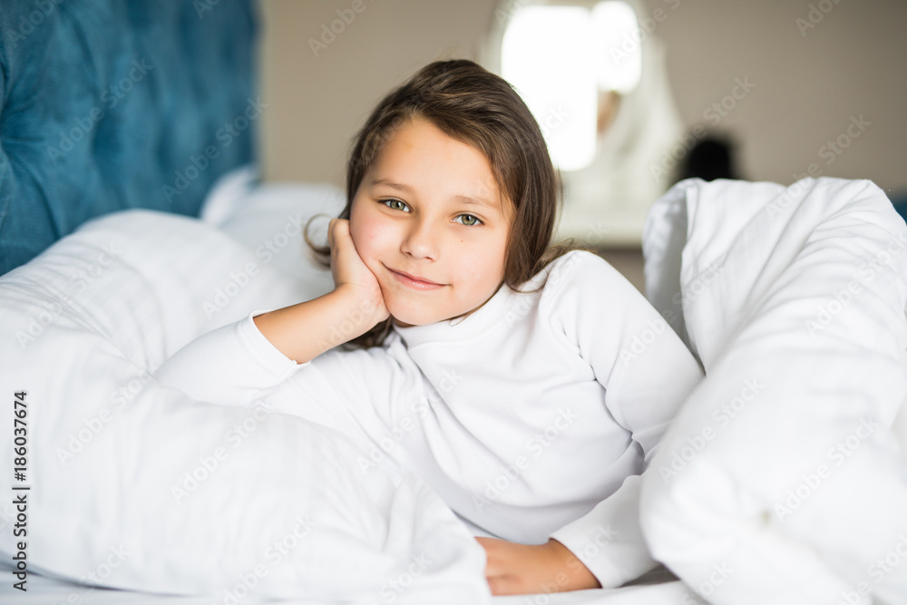 Close-up portrait of beautiful little kid lying on bed with hand under pillow, looking at camera Close-up portrait of beautiful little kid lying on bed with hand under pillow, looking at camera