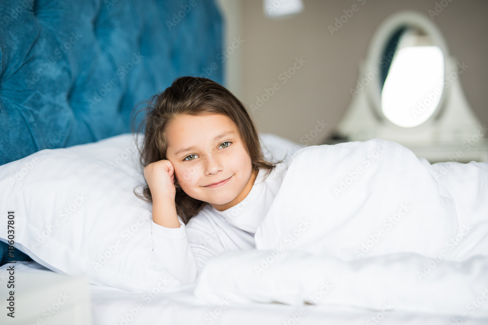 Close-up portrait of beautiful little kid lying on bed with hand under pillow, looking at camera Close-up portrait of beautiful little kid lying on bed with hand under pillow, looking at camera