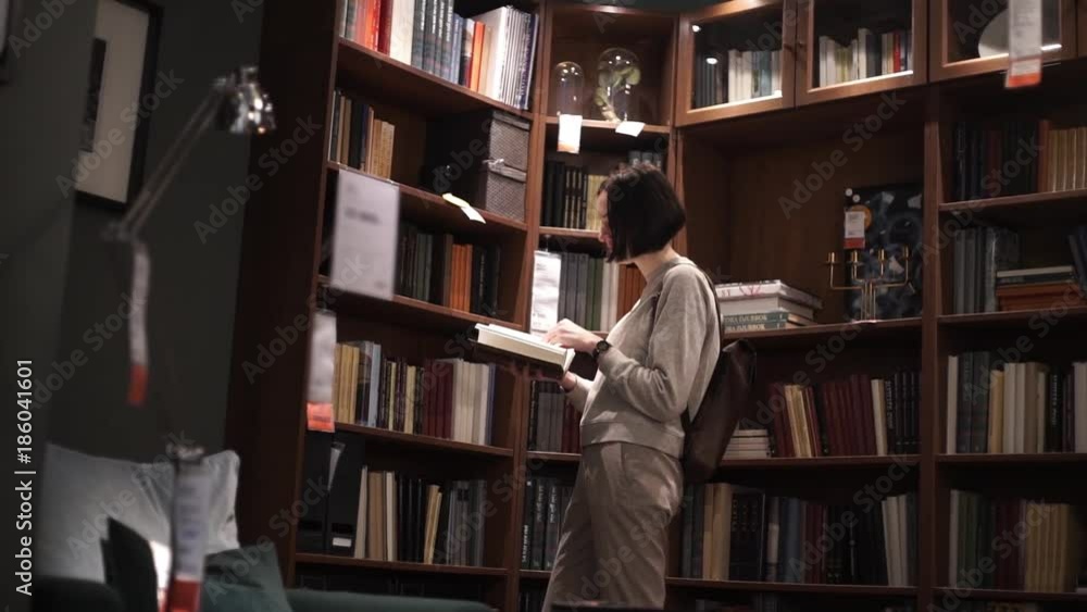 Young girl leafing through magazine while standing near shelves with books Young girl leafing through magazine while standing near shelves with books