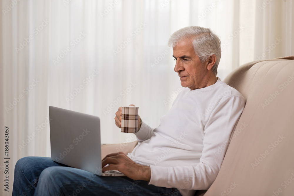 Mature man using laptop during coffee time at home Mature man using laptop during coffee time at home