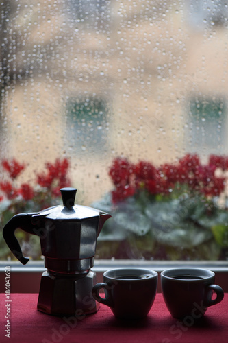 Cups of Hot Coffee and Espresso Machine in front of window raindrops