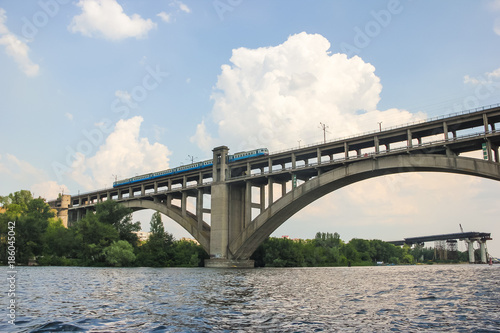A train is riding over a bridge over a river against a blue sky