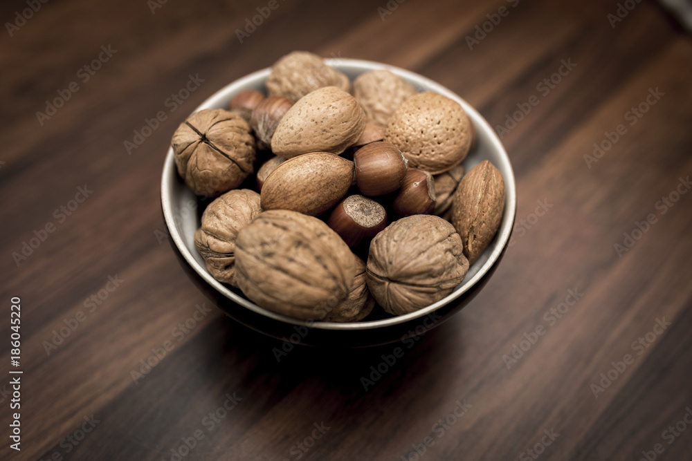 A bowl of mixed whole nuts in their shells including walnuts, hazelnuts, almonds and pecans with a short depth of field A bowl of mixed whole nuts in their shells including walnuts, hazelnuts, almonds and pecans with a short depth of field