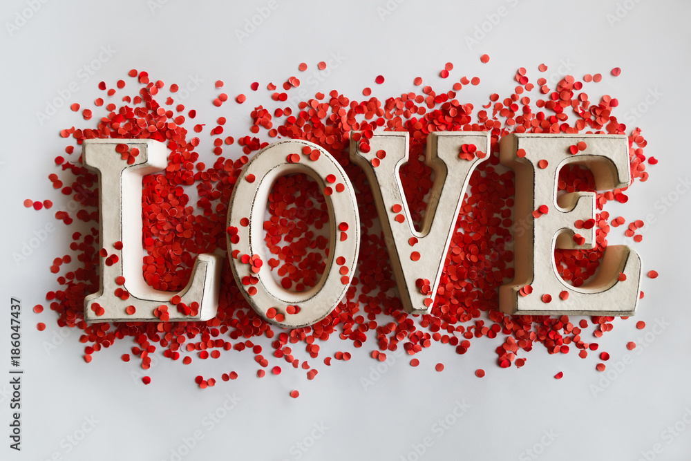 Wooden letters forming word LOVE lying on white surface and sprinkled with red confetti Wooden letters forming word LOVE lying on white surface and sprinkled with red confetti