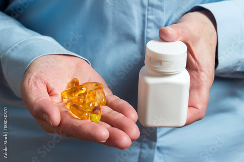 Yellow medication capsules of omega 3, fish oil, healthy supplement pills in the woman palm hand and white plastic bottle in the other hand