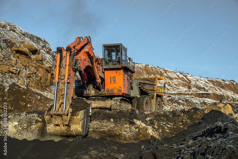 Obraz premium Big yellow dump truck and excavator in coal mine at sunrise 