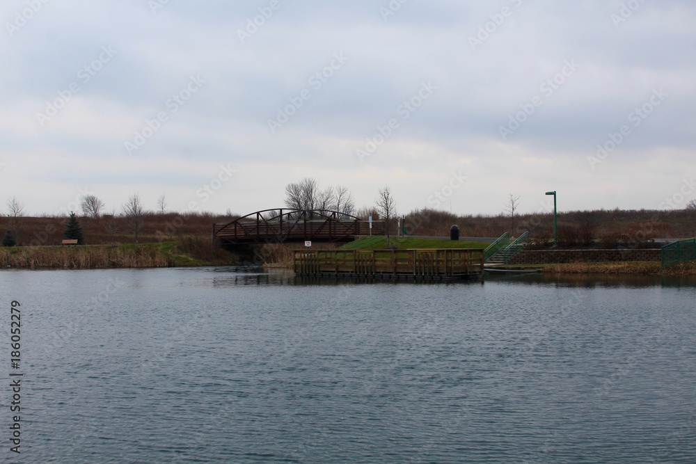 A view of the dock at the lake in the park on a cloudy day.