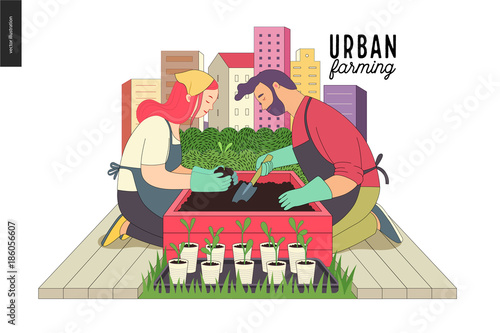 Urban farming, gardening or agriculture. A man and a woman planting out the sprouts to the wooden package bed with a city tower buildings on the background