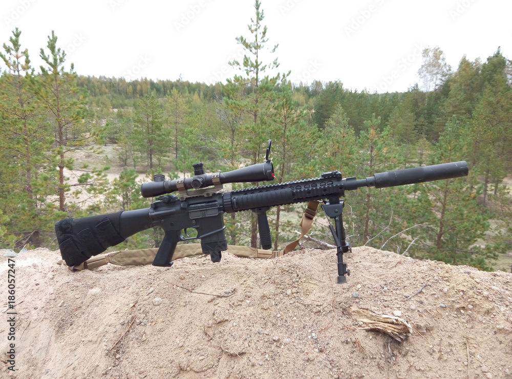 Assault rifle on the background of pine forests and sand Assault rifle on the background of pine forests and sand