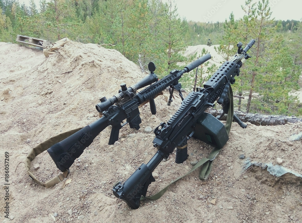Assault rifle and machine gun on the background of pine forests and ...