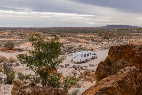 Four wheel drive vehicle and large white caravan camped beside ancient red cliffs in the outback of Australia.