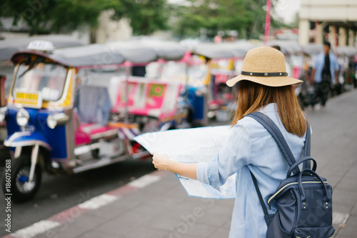 Young woman traveler with sky blue backpack and hat looking the map with tuk tuk Thailand background from china town Bangkok. Traveling in Bangkok Thailand. Travel concept