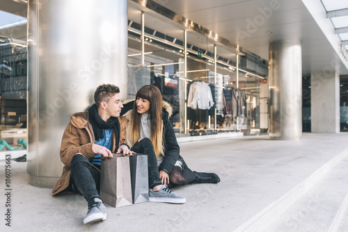 Young beautiful in love couple shopping around the street taking a break seating on the floor .