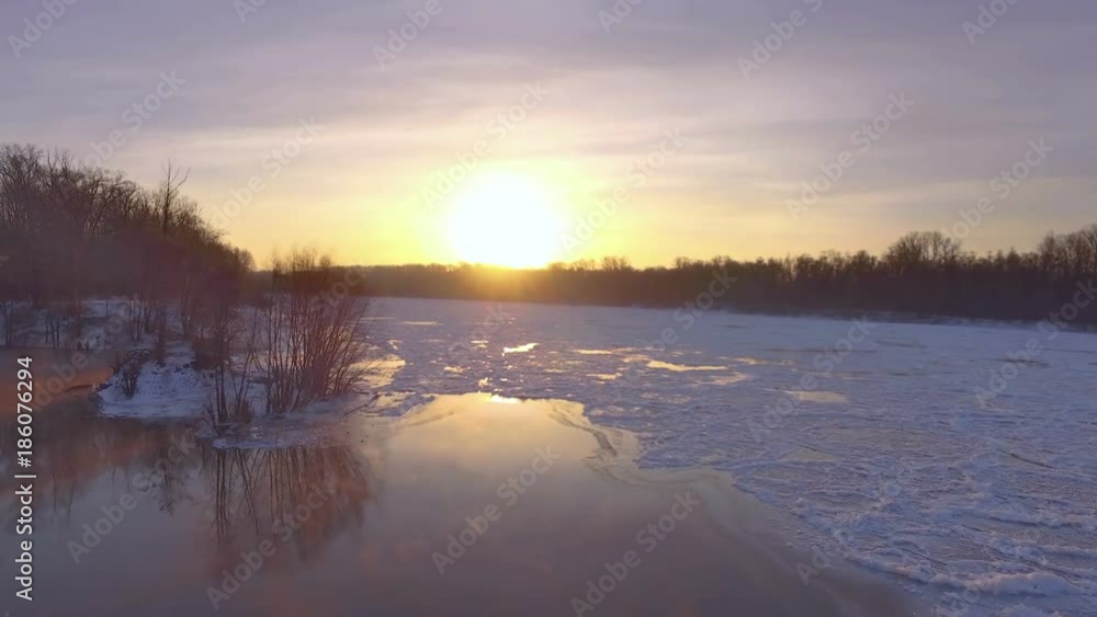 AERIAL: Flight above frozen river to the sun, during dawn. Colorful winter landscape, snowy terrain, trees with hoarfrost on the branches. AERIAL: Flight above frozen river to the sun, during dawn. Colorful winter landscape, snowy terrain, trees with hoarfrost on the branches.