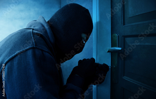 Tela Masked thief using lock picker to open locked door