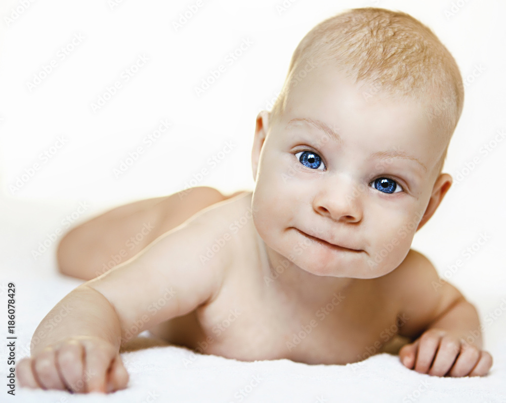 Cute baby on white background with blue eyes smiling lies no white coverlet Cute baby on white background with blue eyes smiling lies no white coverlet