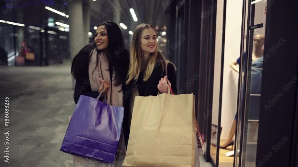 Two cute young adolescent women, heavy loaded with christmas gifts, shopping, while walking along store windows and choosing and admiring the items. Two cute young adolescent women, heavy loaded with christmas gifts, shopping, while walking along store windows and choosing and admiring the items.