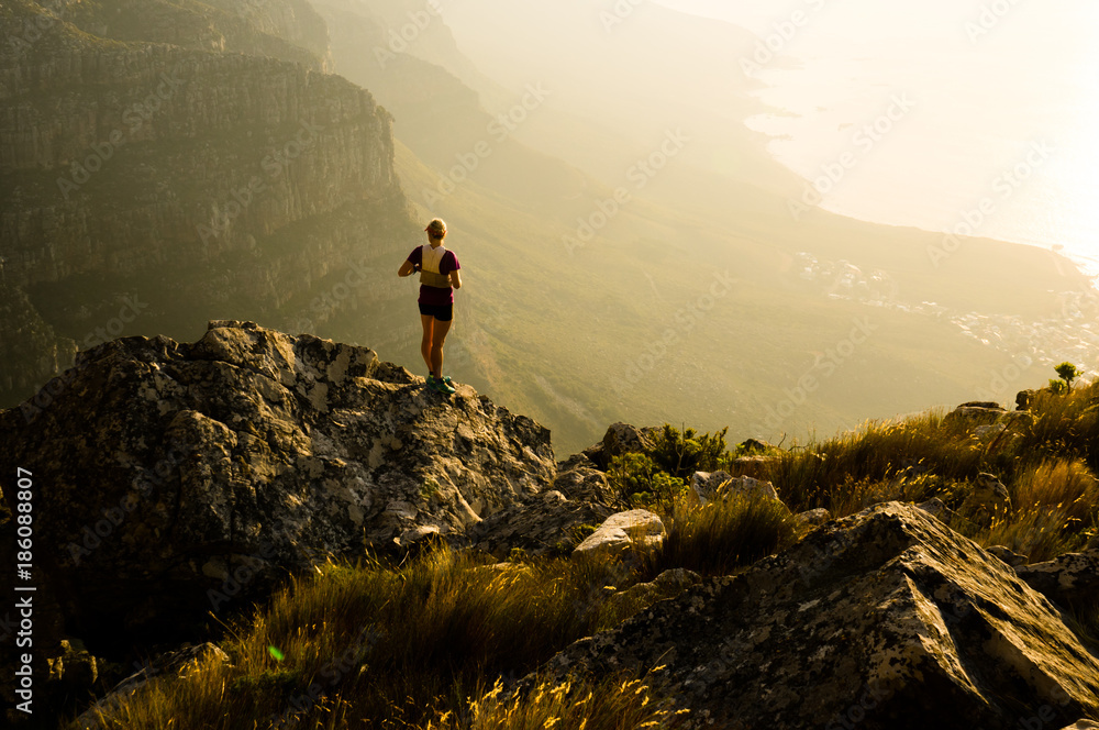 Fototapeta premium Młoda biegaczka szlak dama ogląda zachód słońca ze szczytu góry na półwyspie Cape w Republice Południowej Afryki.