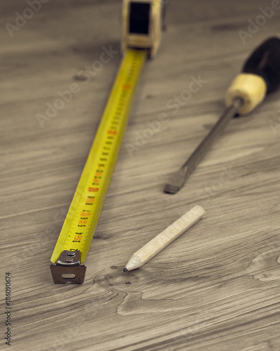Closeup of measure tape, screwdriver and pencil on a wooden background
