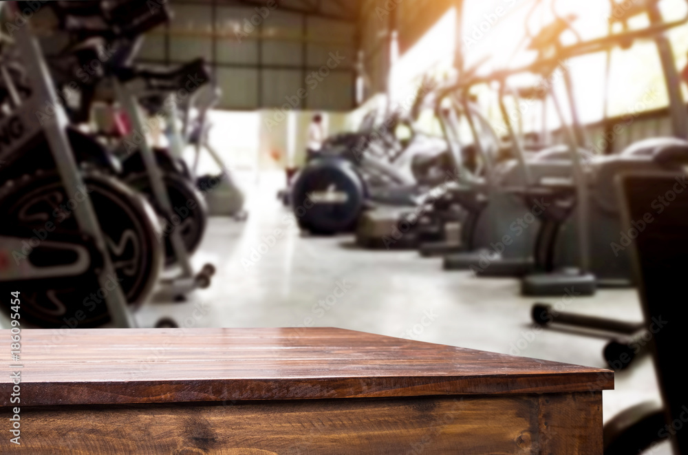 Wooden table on blurred background of fitness gym interior of modern club with equipment for your photomontage or product display. Wooden table on blurred background of fitness gym interior of modern club with equipment for your photomontage or product display.