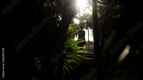 yucatan tropical coast, figure of young women  walking in sun light down stairs in jungle, motion panoram view through big green leaf photo