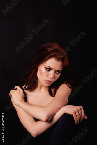 Girl in Studio on dark background. Red hair, great figure. Upset. Holding hand at forehead, in profile