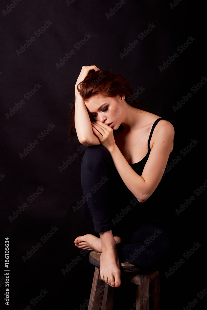 Girl in Studio on dark background. Red hair, great figure. Upset. Holding hand at forehead, in profile Girl in Studio on dark background. Red hair, great figure. Upset. Holding hand at forehead, in profile