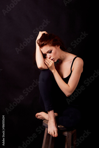 Girl in Studio on dark background. Red hair, great figure. Upset. Holding hand at forehead, in profile