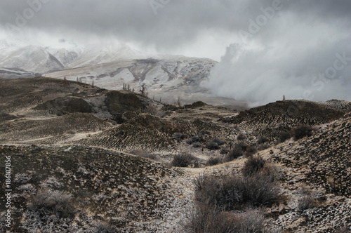 Dramatic winter dark desert steppe on a highland mountain plateau with ranges of  snow peaks on a horizon storm skyline Kurai Altai Mountains Siberia Russia