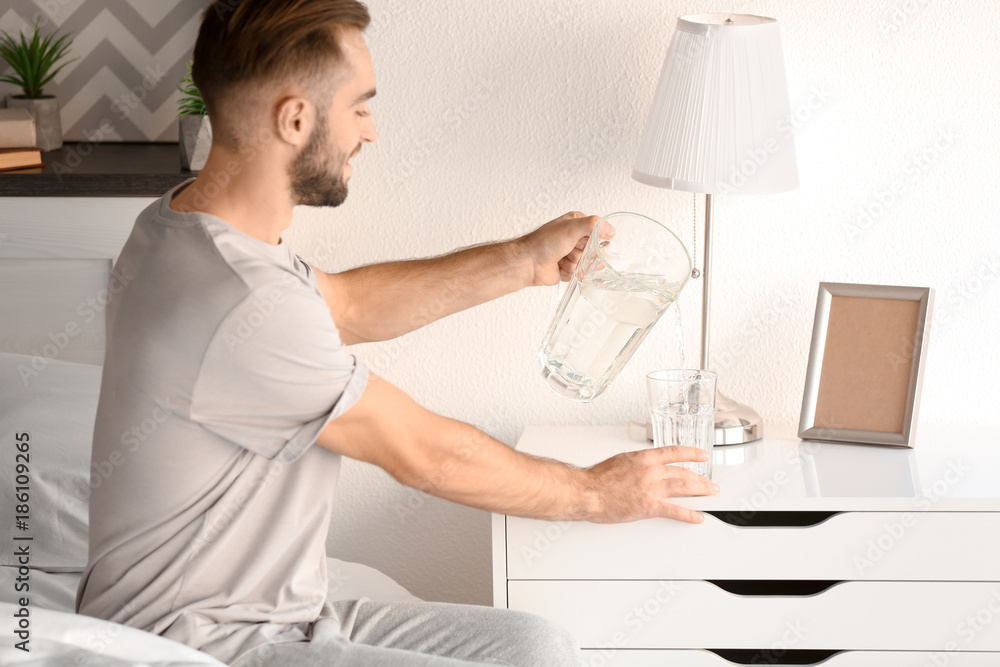Morning of handsome young man pouring water into glass at home Morning of handsome young man pouring water into glass at home
