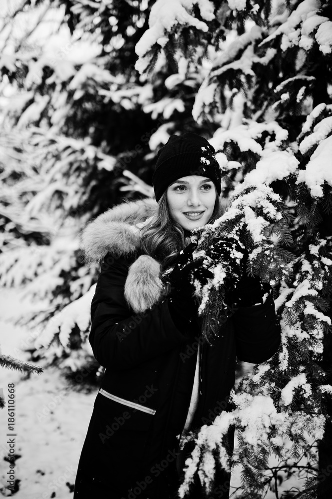 Beautiful brunette girl in winter warm clothing. Model on winter jacket and hat near pine trees.