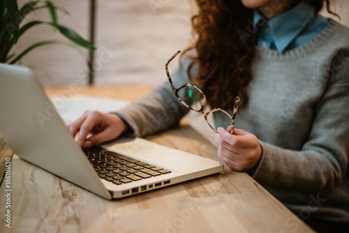 Woman holding glasses and typing on laptop, close up. photo