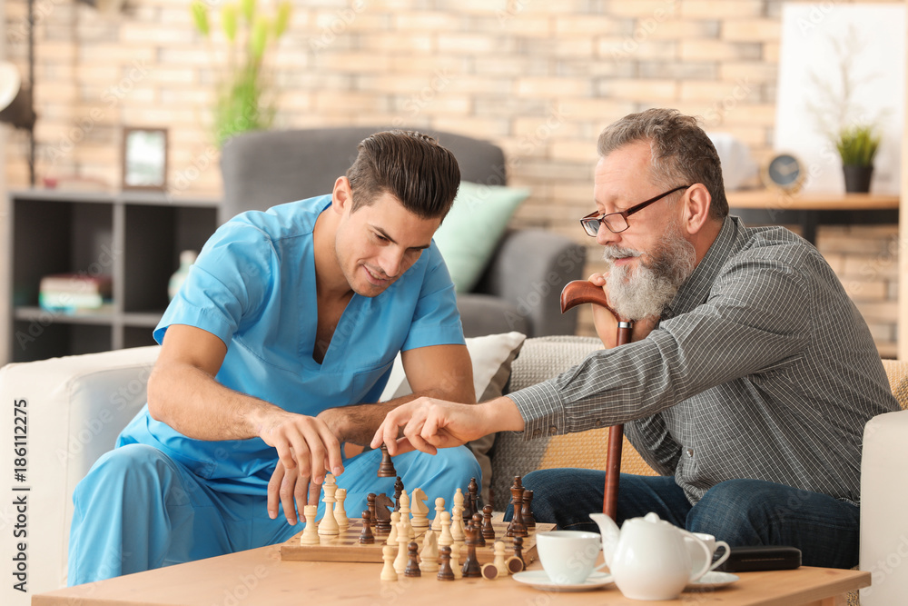 Young caregiver and senior man playing chess at home Young caregiver and senior man playing chess at home