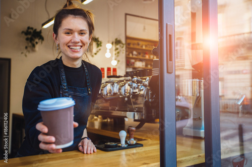 Smiling friendly barista holding disposable cup at coffee shop. Coffee business concept. photo