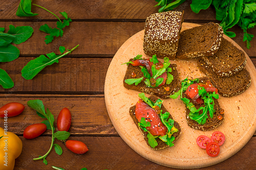 Bruschetta with salmon, red fish, red caviar, arugula and tomatoes on a board. Wooden rustic background. Selective focus. Top view Bruschetta with salmon, red fish, red caviar, arugula and tomatoes on a board. Wooden rustic background. Selective focus. Top view