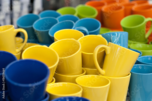 Ceramic Mugs and bowls of different colors in the store on the counter, stand in a row pile. Sale, trade