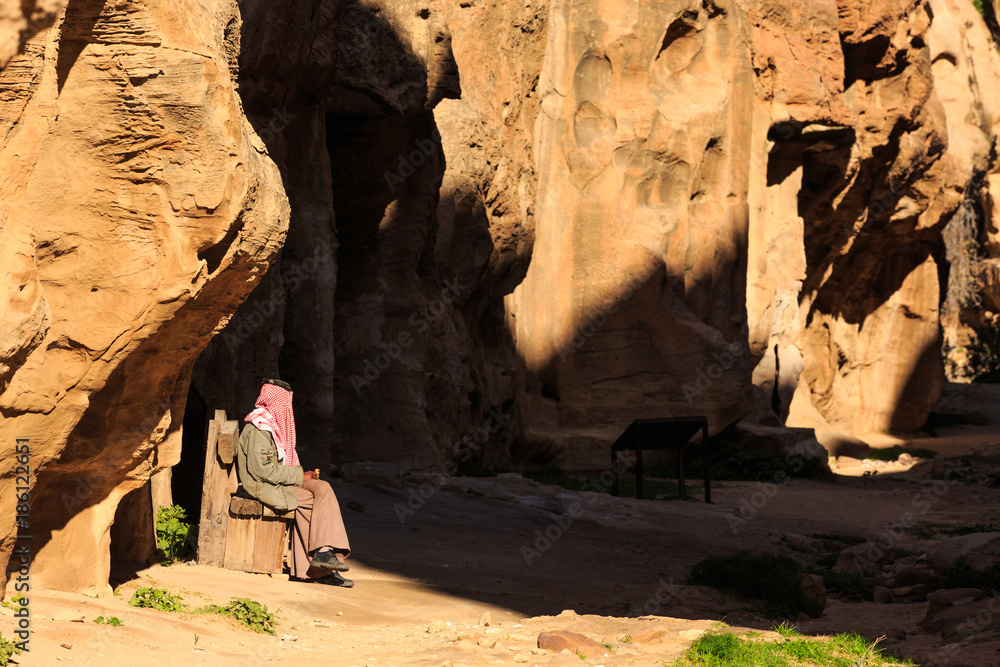 Man stitting in a small passage between the steep rocks at Little Petra in Siq al-Barid, Wadi Musa, Jordan Man stitting in a small passage between the steep rocks at Little Petra in Siq al-Barid, Wadi Musa, Jordan