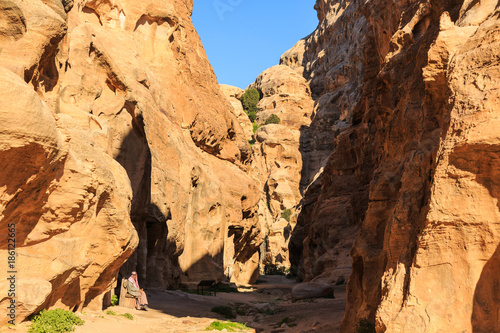 Man stitting in a small passage between the steep rocks at Little Petra in Siq al-Barid, Wadi Musa, Jordan