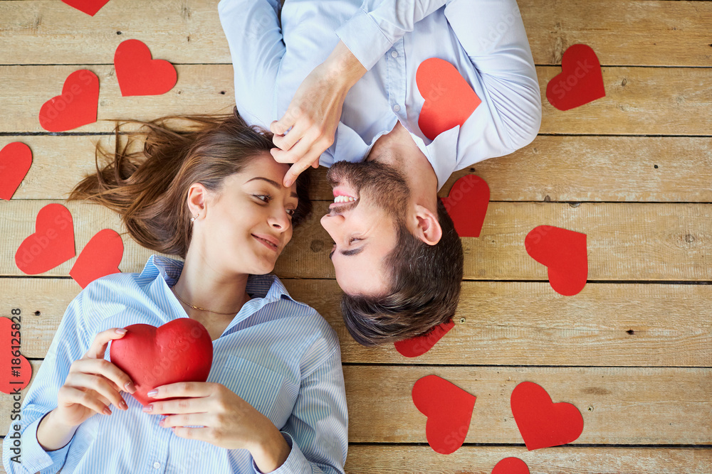 Couple lying on the wooden floor with hearts view from above. Valentine's Day. - obrazy, fototapety, plakaty 