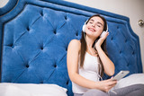 Beautiful young woman listening to music in headphones in bed at home