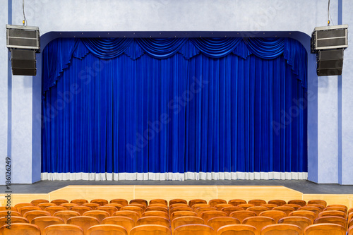 The auditorium in the theater. Blue curtain on the stage. Blue-brown chair. Room without people.