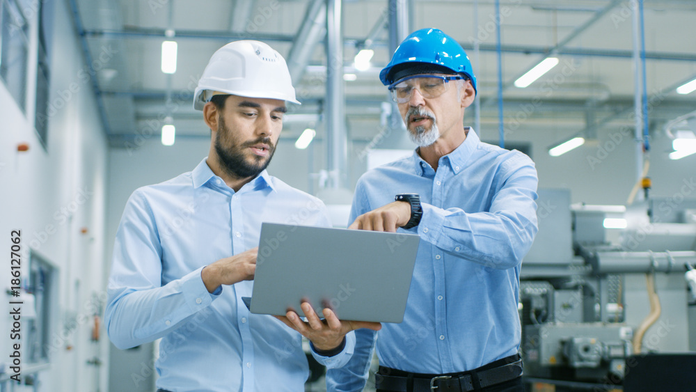 Head of the Project Holds Laptop and Discusses Product Details with Chief Engineer while They Walk Through Modern Factory. Head of the Project Holds Laptop and Discusses Product Details with Chief Engineer while They Walk Through Modern Factory.