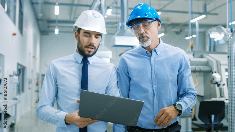 Head of the Project Holds Laptop and Discusses Product Details with Chief Engineer while They Walk Through Modern Factory. Head of the Project Holds Laptop and Discusses Product Details with Chief Engineer while They Walk Through Modern Factory.