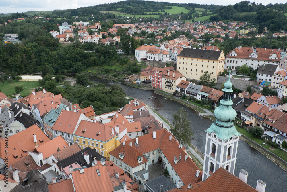View of the charming medieval town, Cesky Krumlov, from the castle tower. Looking over the town from high up, Church of St Jost overlooking the Vltava River flowing through the town green hills beyond