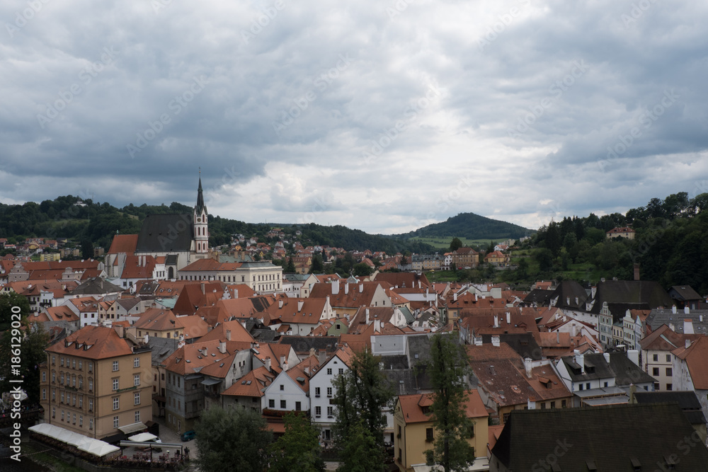View of the charming medieval town, Cesky Krumlov, from the castle. St Vitus Church and the town of Cesky Krumlov, green mountains and stormy sky. Red roofed houses in charming town in Europe. View of the charming medieval town, Cesky Krumlov, from the castle. St Vitus Church and the town of Cesky Krumlov, green mountains and stormy sky. Red roofed houses in charming town in Europe.