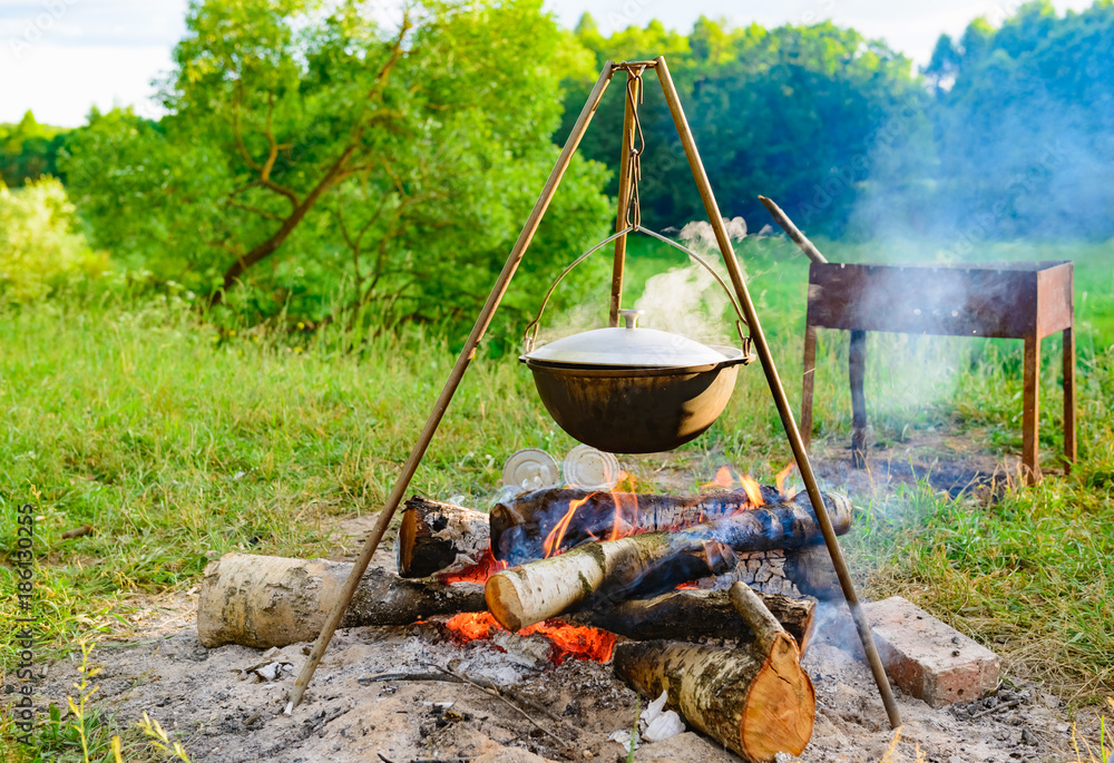 a camp-steaky sooty food bowl hanging on a tripod over a fire a camp-steaky sooty food bowl hanging on a tripod over a fire